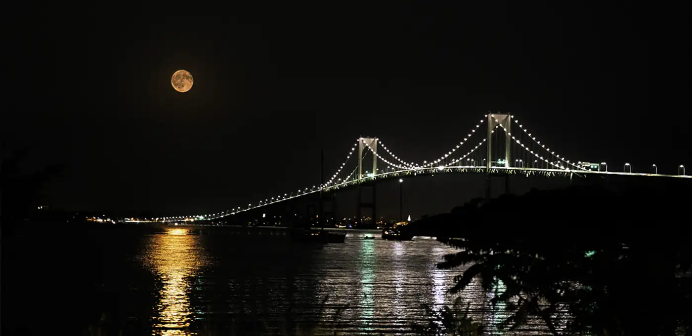The Newport Bridge lit at night under a full moon